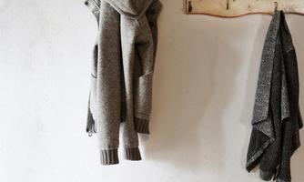 A cozy setting with a wooden frame on which gray sweaters hang. Below, a soft white sheepskin lies on a wooden bench.