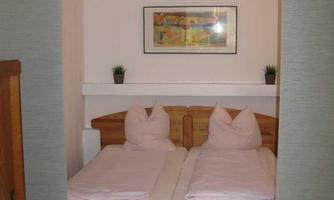 A cozy bedroom with two single beds and modern pillows. A colorful painting hangs on the wall above a simple shelf.