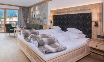 A cozy hotel room with a double bed and wooden decor. There is a balcony with a view of the mountains and a stylish interior.
