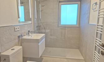 A modern bathroom with bright tiles and a large shower. There is a sink and a window that lets in natural light.