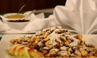 A plate with a delicious dessert, sprinkled with powdered sugar and served with apple slices. In the background, sauces in bowls can be seen.