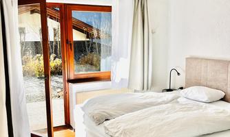 A cozy bedroom with a single bed and red curtains. Next to the bed, there is a laptop on a small table.