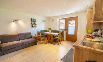 A cozy living room with a sofa and a dining table. The bright, open kitchen is well-equipped and the window lets in a lot of light.