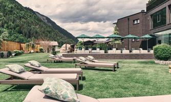 A beautiful garden with sun loungers and sun umbrellas. In the background, there are mountains and a modern building.