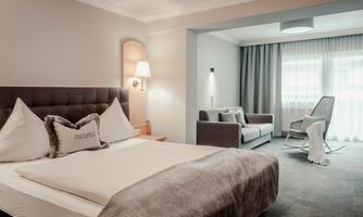 An elegant bedroom with a large, comfortable bed and soft colors. In the background, there is a cozy sitting area with a sofa and armchair.