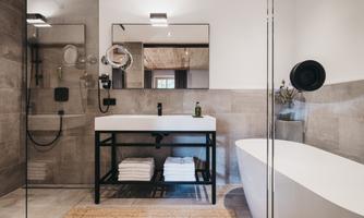 A modern bathroom with a freestanding bathtub and an elegant sink. The walls are in neutral tones, and there are clean towels on a shelf.