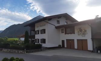 A beautiful building in Bavarian style, surrounded by green landscapes. In the background, mountains and a clear sky can be seen.