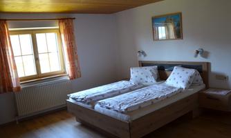 A bright bedroom with two single beds and hardwood flooring. Large windows let in plenty of daylight.
