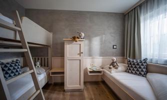 A modern children's room with a bunk bed and a cozy seating area. The walls are painted in soft shades of grey, and the room is bright and inviting.