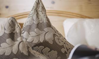 A couple of decorative cushions with an elegant pattern are lying on a bed. The background features a cozy wooden wall.