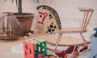 A cheerful children's room with a wooden rocking horse and colorful building blocks. In the background, there is a pot with a plant.