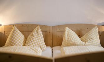 A cozy double bed with checkered pillows in a wooden frame. The soft lighting creates a relaxed atmosphere.