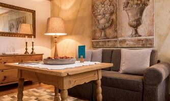 A cozy room with a wooden table, a sofa, and decorative paintings on the wall. A lamp and a sideboard give the space an inviting atmosphere.