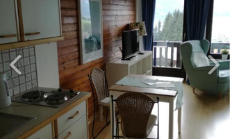 A cozy holiday apartment with a modern kitchenette and a dining table. In the background, a television and a comfortable armchair can be seen.