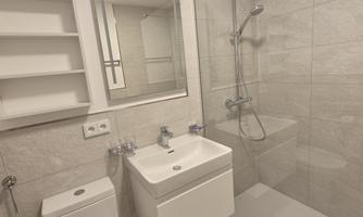 A modern bathroom with a shower and a sink. The walls are tiled in neutral color tones, and there is a large mirror.
