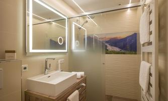 A modern bathroom with a clear shower partition and a stylish sink. Illuminated mirrors and a mountain motif create a relaxing atmosphere.