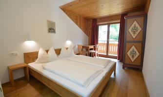 A cozy bedroom with wood decor and a large window. There are two beds, a table, and a wardrobe.