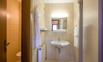 A simple bathroom with white tiles and a sink. There is a mirror, towels, and a toilet area.
