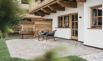 A cozy terrace with a stone grill and seating furniture. Surrounded by well-maintained lawn and wooden cladding.