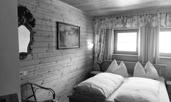 A cozy bedroom with wood paneling and a big bed. A mirror hangs on the wall and there is a chair in the corner.