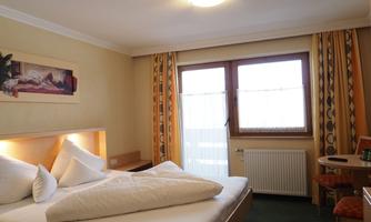 A cozy hotel room with a double bed and light curtains. The room is simply designed but inviting.