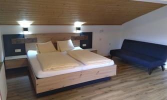 A cozy bedroom with a double bed and a wooden ceiling. The room also features a black couch.