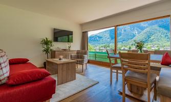 A modern living room with a red sofa and wooden furniture. Large windows provide a view of the mountains and nature.