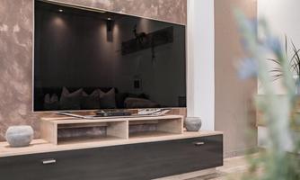 A modern living room with a large TV on the wall. The TV is on a simple wooden cabinet with decoration.