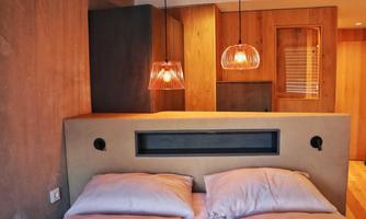 A modern bedroom with a cozy double bed and stylish pendant lights. The walls are made of light wood, creating a warm atmosphere in the room.