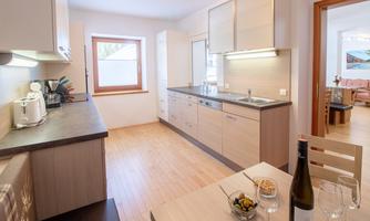 A modern kitchen with bright wood cabinets and elegant appliances. A dining table with wine and snacks invites you to linger.