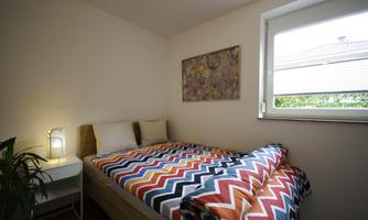 A cozy bedroom with a single bed and colorful bedding. A nightstand and a window create a bright atmosphere.