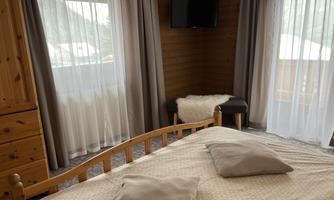 A cozy bedroom with a large bed and two windows. The walls are made of wood, and there is a TV on the wall.