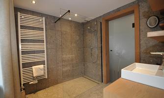 A modern bathroom with a glass shower and stone tiles. Visible are a towel holder and a wooden sink.