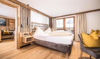 A modern hotel room with a large bed and cozy furnishings. The warm wood and beige tones create an inviting atmosphere.