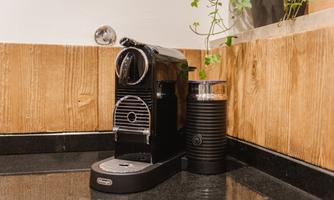 A modern Nespresso machine stands on a black countertop. In the background, wooden paneling and a small plant can be seen.