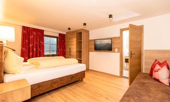 A modern hotel room with wood paneling and large windows. The furnishings include a comfortable bed, a television, and a cozy seating area.