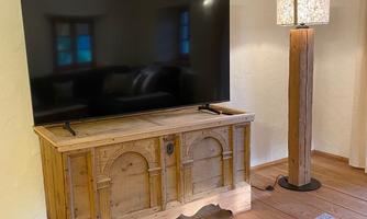 A living room with a large flat-screen TV and a wooden dresser. Next to the dresser stands a stylish floor lamp.