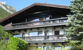 A charming chalet in the mountains with wooden cladding and several balconies. Surrounded by green trees and beautiful scenery.