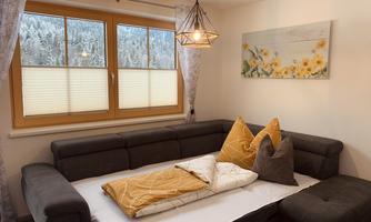 A cozy living room with a gray sofa and yellow cushions. Through the window, a snowy landscape can be seen.