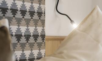A stylish interior design featuring a patterned wall and a modern wall lamp. In the foreground, soft cushions are visible.
