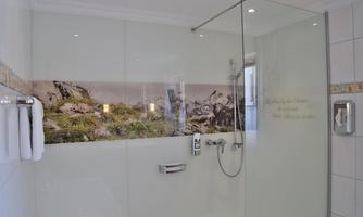 A modern bathroom with a spacious glass shower cabin. On the wall, a colorful photograph of a landscape can be seen.