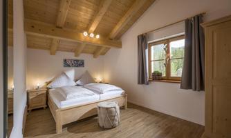 A cozy bedroom with a double bed and wooden furniture. Large windows ensure plenty of daylight and a pleasant atmosphere.