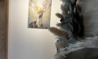 A bright hallway with a piece of artwork on the wall depicting a deer. In the foreground, a decorative wreath made of plants can be seen.