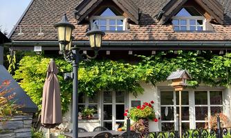 A charming house with a green entrance and large windows. Next to the building stands a lamp and an umbrella.