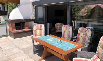 A cozy terrace with a wooden table and comfortable chairs. In the background, there is a grill.
