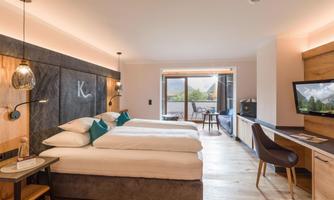 A modern hotel room with two beds and elegant furnishings. Large windows provide a view of the surrounding landscape.