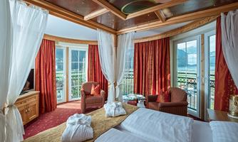 An elegant hotel room with a balcony and large windows. The decor is cozy and stylish with red curtains and a wooden ceiling.