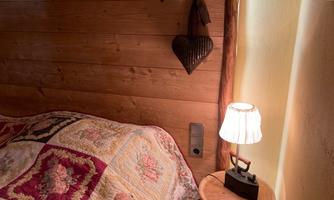 A cozy bedroom with wooden paneling and a colorful duvet cover. Next to the bed is a small lamp and a nostalgic iron on a table.