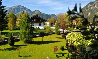 A picturesque landscape with green meadows and trees. In the background, impressive mountains and traditional houses can be seen.