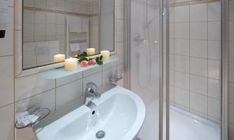 A modern bathroom with a shower and a sink. Candles and flowers are on the sink as decoration.